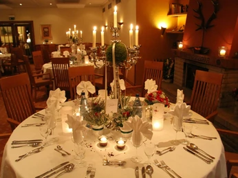 Hirschsprung_Kaminzimmer.jpg Ein festlich gedeckter Tisch mit Kerzenständern und Stoffservietten vor einem Kamin in einem eleganten Raum.