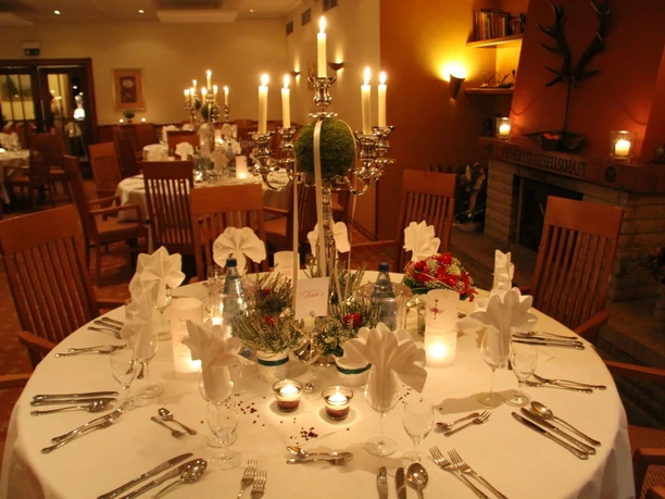 Hirschsprung_Kaminzimmer.jpg Ein festlich gedeckter Tisch mit Kerzenständern und Stoffservietten vor einem Kamin in einem eleganten Raum.