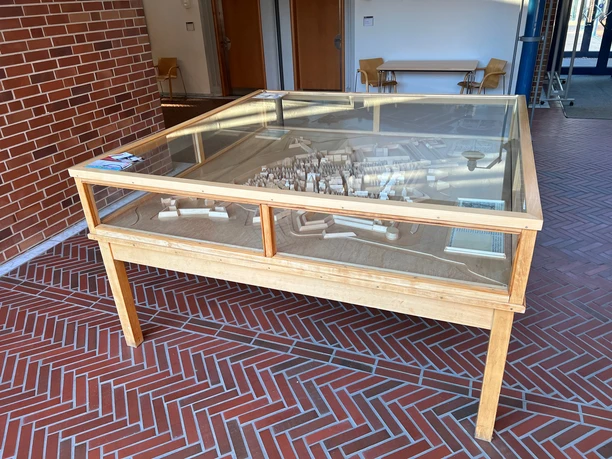 Stadtmodell im Rathaus Ein hölzerner Tisch mit einem unter Glas geschützten Stadtmodell aus weißem Material in einem kalten Flur.