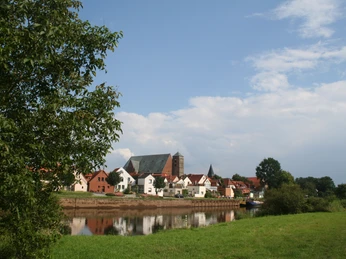 Im Bild erstreckt sich die malerische Stadtkulisse Verdenners am Fluss, umgeben von üppigem Grün.