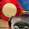 Ein altes Polizeischild mit einem Miniaturmodell eines grünen VW Käfer Polizeiautos im Vordergrund.