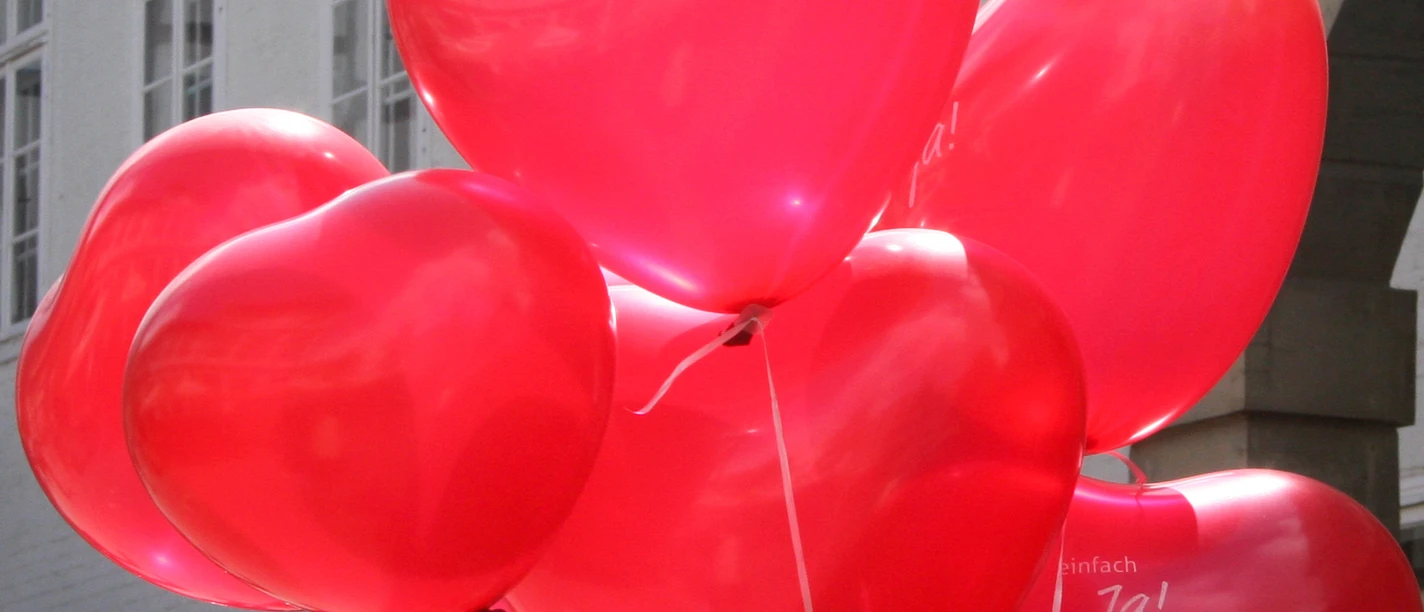 Rote Herzballons schweben vor weißen Backsteinwänden, sorgen für eine fröhliche, festliche Stimmung.
