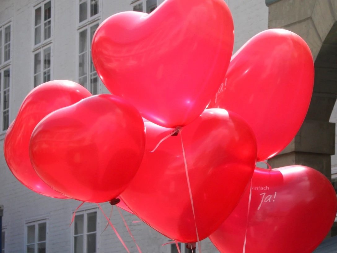 Ballons Rote Herzballons schweben vor weißen Backsteinwänden, sorgen für eine fröhliche, festliche Stimmung.