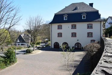Burghaus Bielstein Ein historisches dreistöckiges Gebäude mit Schieferdach, umgeben von einer gepflasterten Straße.