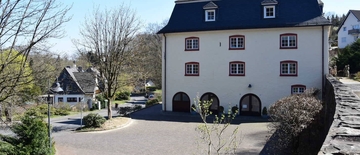 Burghaus Bielstein Ein historisches dreistöckiges Gebäude mit Schieferdach, umgeben von einer gepflasterten Straße.