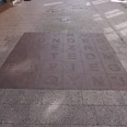 Bodenfliesen mit eingravierten Buchstaben und Wörtern, von Sonnenlicht und Schatten bedeckt.