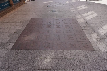 Bodenfliesen Bodenfliesen mit eingravierten Buchstaben und Wörtern, von Sonnenlicht und Schatten bedeckt.