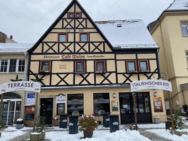 Café Welyn Fachwerkhaus mit Café und Eisdiele, beschneit, mit Schildern "Terrasse" und "Italienisches Eis", umgeben von winterlicher Atmosphäre.