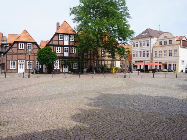 Fachwerkhäuser umgeben einen gepflasterten Platz in Verden, Niedersachsen, unter blauem Himmel.