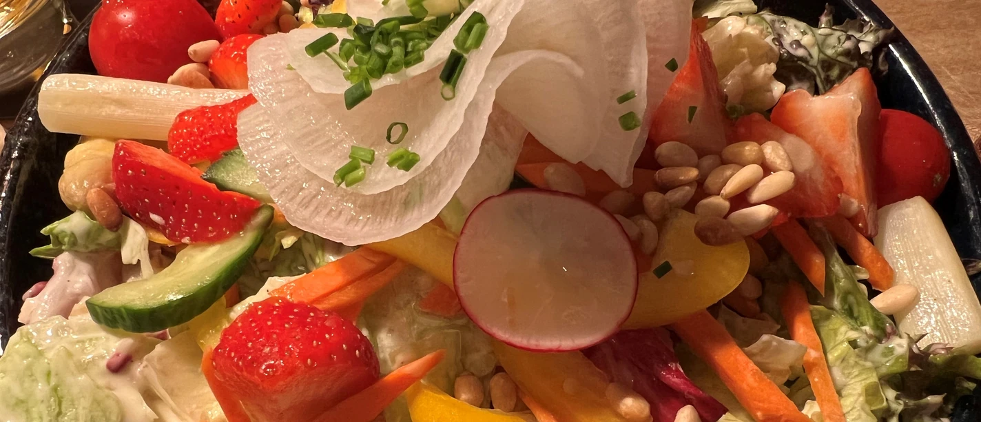 Ein bunter Salatteller mit Erdbeeren, Radieschen und Paprika, garniert mit Schnittlauch und Pinienkernen.