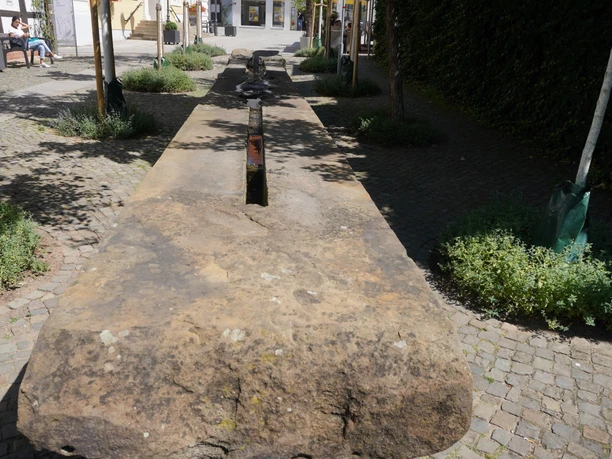 Brunnen Verden Langer Steinbrunnen auf gepflastertem Platz in Verden, umgeben von Bäumen und Sitzbänken.