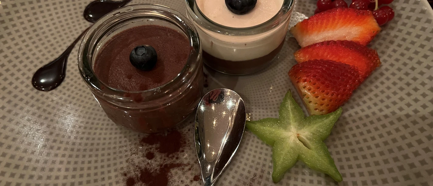 Two dessert glasses with chocolate mousse and berries on an artfully arranged plate.