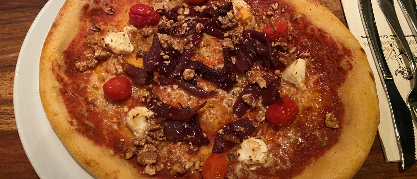 Pizza met een knapperige korst, belegd met geitenkaas, kerstomaatjes, walnoten en rode pesto.