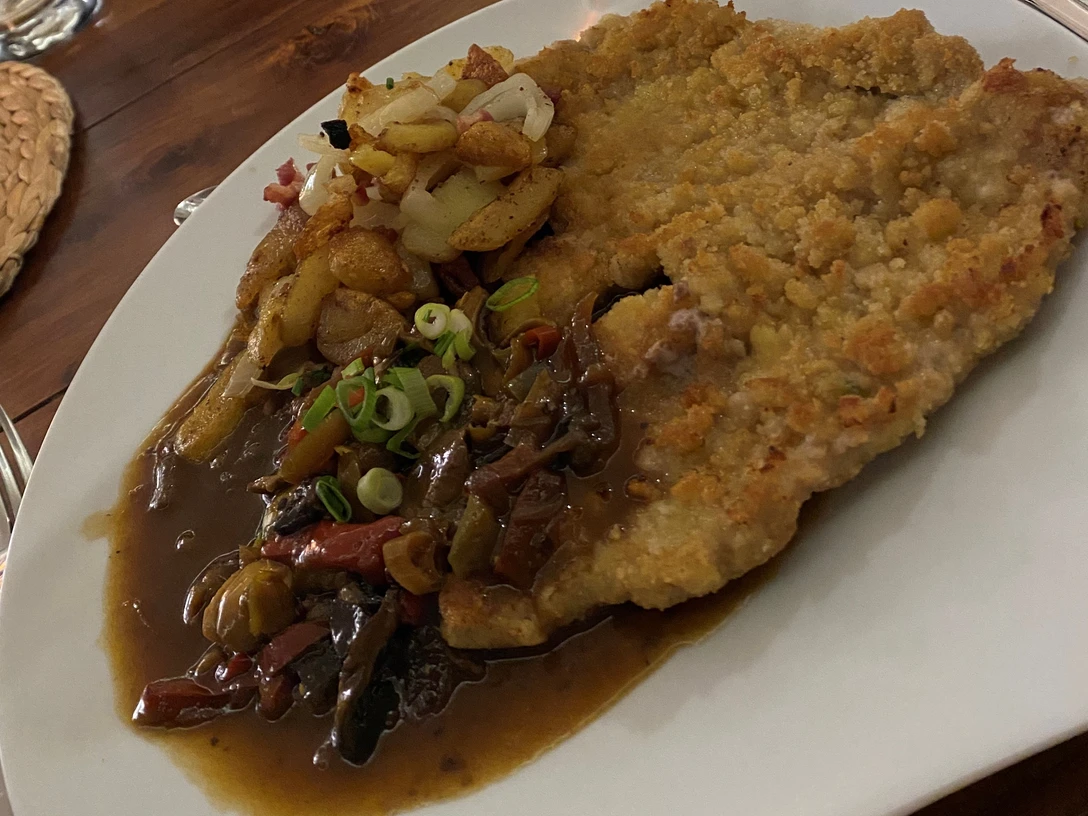 Ein Teller mit Jägerschnitzel, Bratkartoffeln, Soße und Gemüsegarnitur, daneben ein Rotweinglas.A plate with Jägerschnitzel, fried potatoes, gravy and vegetable garnish, next to it a glass of red wine.En tallerken med Jägerschnitzel, stegte kartofler, sovs og grøntsagsgarniture, ved siden af et glas rødvin.Een bord met Jägerschnitzel, gebakken aardappelen, jus en groentegarnituur, daarnaast een glas rode wijn.