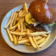 Burger Ein saftiger Burger mit geschmolzenem Käse und goldbraunen Pommes Frites auf einem Keramikteller.