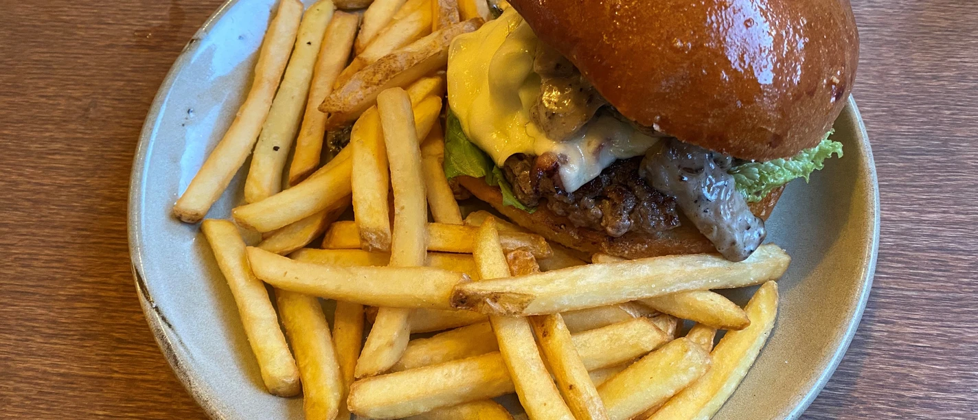 Burger Ein saftiger Burger mit geschmolzenem Käse und goldbraunen Pommes Frites auf einem Keramikteller.