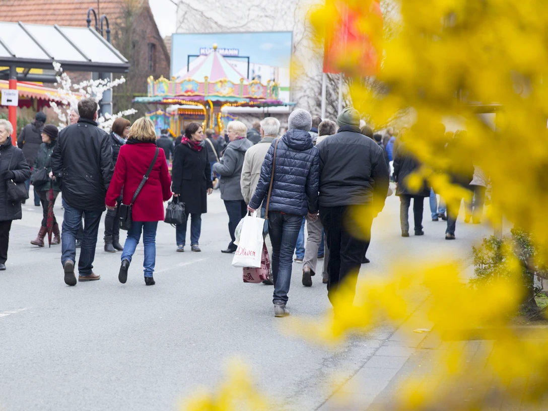 Frühlingsmarkt in der Delbrücker Innenstadt Menschen bummeln auf einem belebten Frühlingsmarkt; bunte Verkaufsstände und gelbe Blüten im Vordergrund.