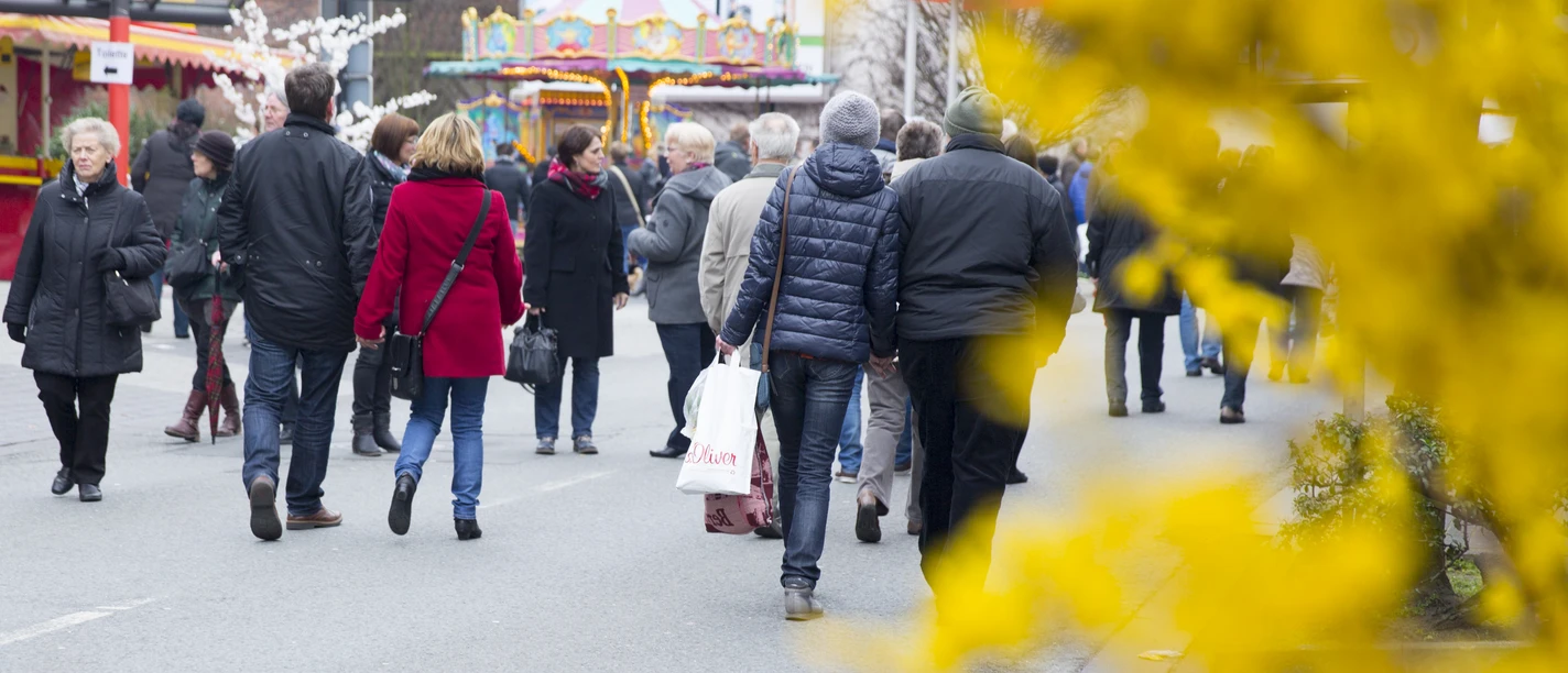 Frühlingsmarkt in der Delbrücker Innenstadt Menschen bummeln auf einem belebten Frühlingsmarkt; bunte Verkaufsstände und gelbe Blüten im Vordergrund.