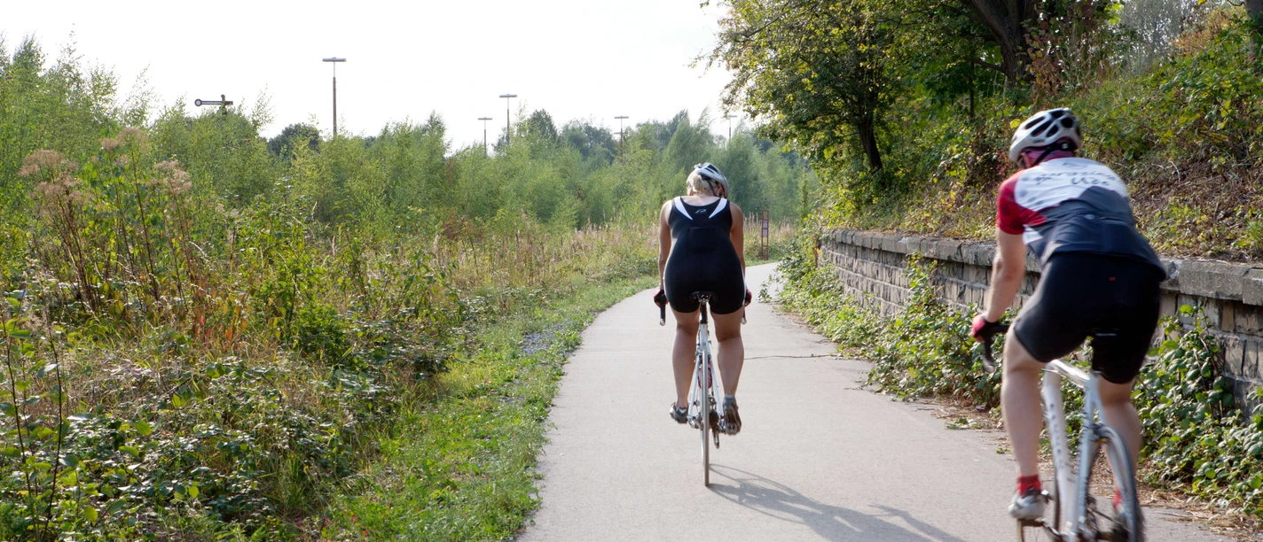 Unterwegs auf dem PanoramaRadweg niederbergbahn Zwei Radfahrende auf dem PanoramaRadweg Niederbergbahn, umgeben von grüner Natur und Bäumen.