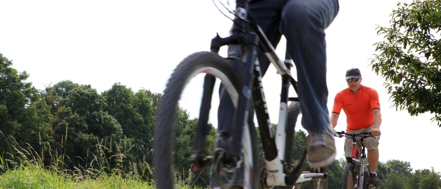 Ausflug auf dem PanoramaRadweg niederbergbahn Zwei Personen radeln entlang eines Schotterwegs, umgeben von grüner Vegetation, bei sonnigem Wetter.