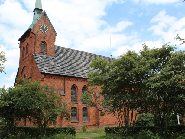 Bartholomäus-Kirche Backsteinkirche mit grünem Glockenturm, gotischen Fenstern und Uhr vor einem bewölkten Himmel.