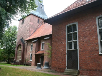 St.-Marcellus-Kirche Asendorf Backsteinkirche mit Turm und Glocken im Vordergrund, eingebettet in eine grüne Parkanlage.ungerade