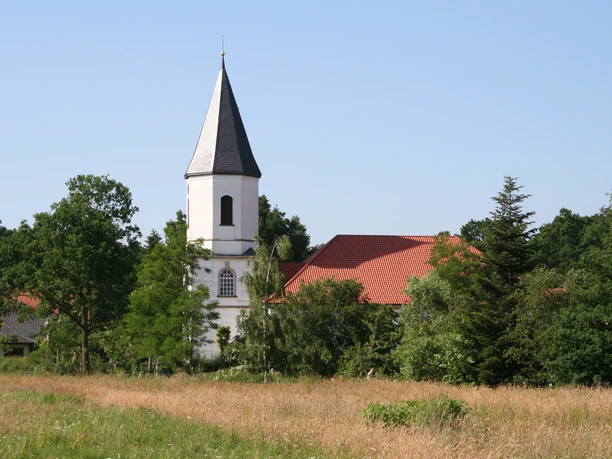 Catharinenkirche Martfeld Eine weiße Kirche mit spitzem Turm schmiegt sich in eine grüne Landschaft und unter blauen Himmel.