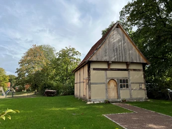 Pastorenhaus Martfeld Historisches Fachwerkhaus mit spitzem Dach, umgeben von Bäumen und einer Rasenfläche bei Sonnenschein.
