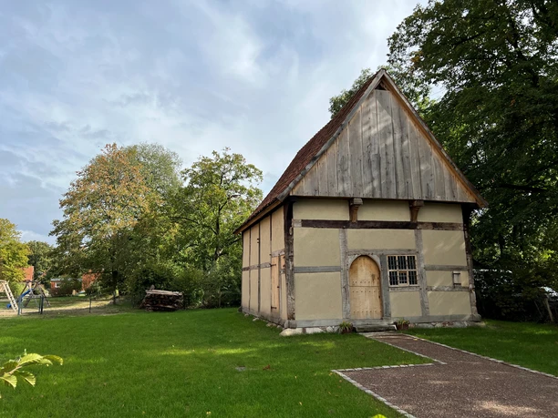 Pastorenhaus Martfeld Historisches Fachwerkhaus mit spitzem Dach, umgeben von Bäumen und einer Rasenfläche bei Sonnenschein.
