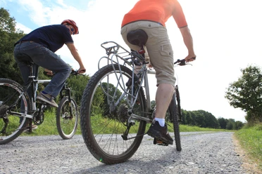 Fahrradfahren auf dem PanoramaRadweg niederbergbahn Zwei Personen fahren auf Fahrrädern über einen Schotterweg im Grünen, umgeben von Bäumen.