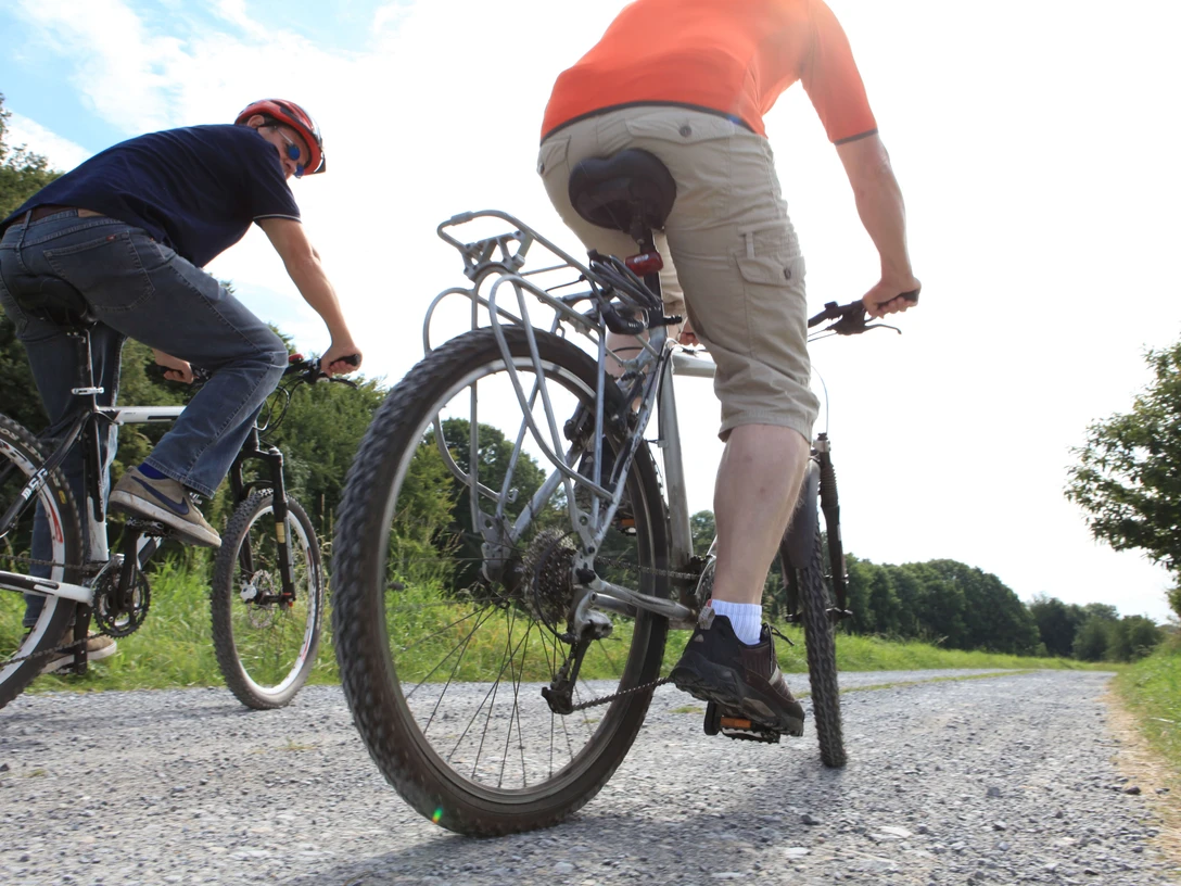 Fahrradfahren auf dem PanoramaRadweg niederbergbahn Zwei Personen fahren auf Fahrrädern über einen Schotterweg im Grünen, umgeben von Bäumen.