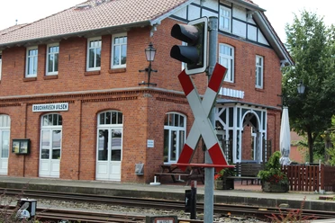 Ein rotes Backsteingebäude des Bahnhofs Bruchhausen-Vilsen mit charakteristischen weißen Fensterrahmen und einem Bahnübergangsschild im Vordergrund.