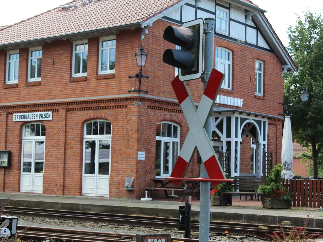 Bahnhof Bruchhausen-Vilsen Ein rotes Backsteingebäude des Bahnhofs Bruchhausen-Vilsen mit charakteristischen weißen Fensterrahmen und einem Bahnübergangsschild im Vordergrund.