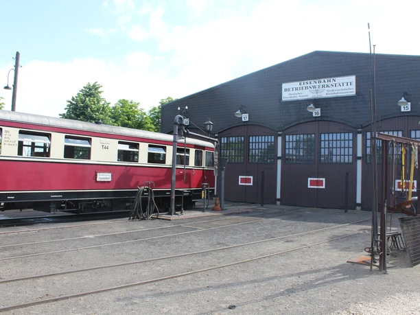 Ein roter historischer Zug steht vor einem traditionellen Fachwerkgebäude des Eisenbahnmuseums.