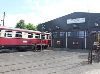 Museumseisenbahn Bruchhausen-Vilsen Ein roter historischer Zug steht vor einem traditionellen Fachwerkgebäude des Eisenbahnmuseums.