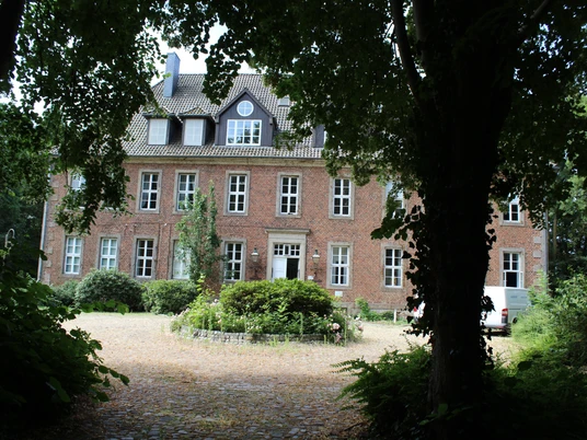 Amtshof 2 Bruchhausen-Vilsen Backsteingebäude in einem üppig begrünten Umfeld mit Kopfsteinpflaster im Vordergrund.