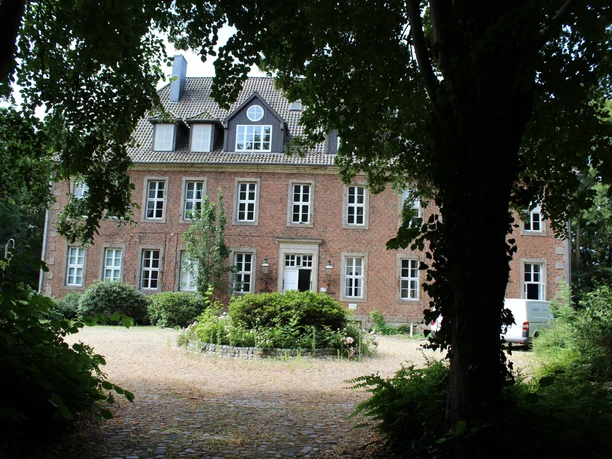 Amtshof 2 Bruchhausen-Vilsen Backsteingebäude in einem üppig begrünten Umfeld mit Kopfsteinpflaster im Vordergrund.