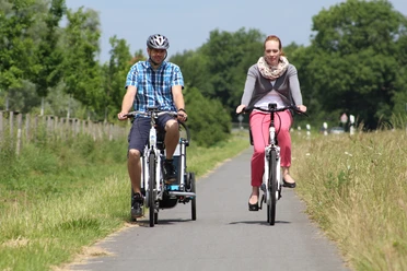 Radfahren in der Mittelweser-Region Zwei Radfahrer genießen eine Fahrt auf einem asphaltierten Weg, umgeben von grüner Natur und Bäumen.