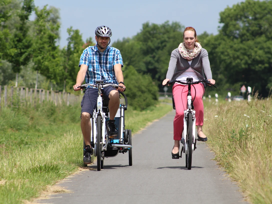 Radfahren in der Mittelweser-Region Zwei Radfahrer genießen eine Fahrt auf einem asphaltierten Weg, umgeben von grüner Natur und Bäumen.