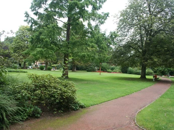 Weitläufiger Kurpark mit grünem Rasen, umrahmt von hohen Bäumen und einem geschwungenen Kiesweg.