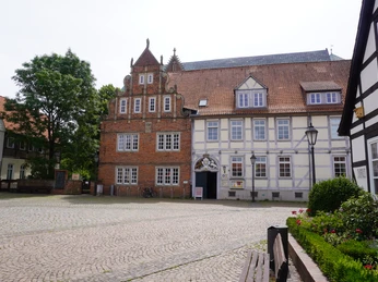 Historisches Backsteingebäude mit verzierten Giebeln und weiß-blauem Fachwerk im ländlichen Umfeld.