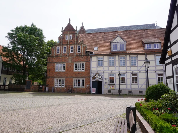 Lugenstein Verden Historisches Backsteingebäude mit verzierten Giebeln und weiß-blauem Fachwerk im ländlichen Umfeld.