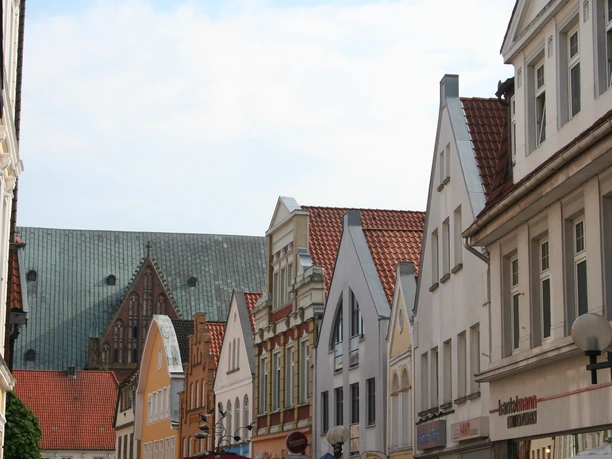 A street scene in Verden, with gabled houses in the foreground and a church with a green roof in the background.