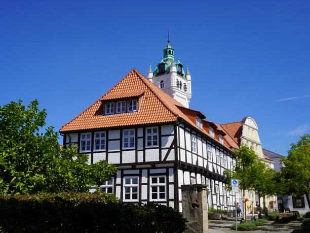 Fachwerkhaus in Verden mit markantem Turm vor strahlend blauem Himmel und grünen Bäumen im Vordergrund.