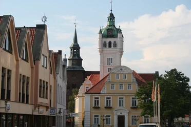 Historisches Rathaus von Verden mit weißem Turm und Uhr, umgeben von Fachwerkhäusern und Bäumen.