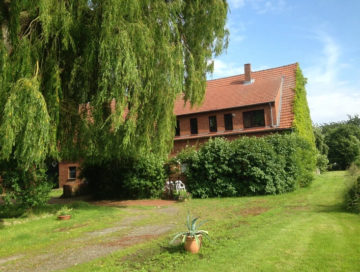 Gruene-Ferienwohnung_1.JPG Ziegelsteingebäude mit großem, bewachsenem Giebel und Grünfläche; einladende ländliche Ruhe.