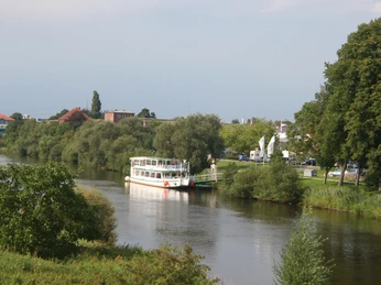 Weißes Ausflugsschiff auf der Aller mit grüner Uferböschung und Bäumen im Hintergrund an einem Sonnentag.