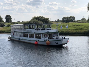 Ein weiß-grünes Ausflugsschiff, die MS "Stadt Verden", fährt auf einem ruhigen Fluss in grüner Landschaft.