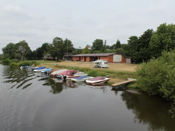 Eine ruhige Flusslandschaft mit Booten am Ufer und einem Vereinshaus im Hintergrund in Verden.