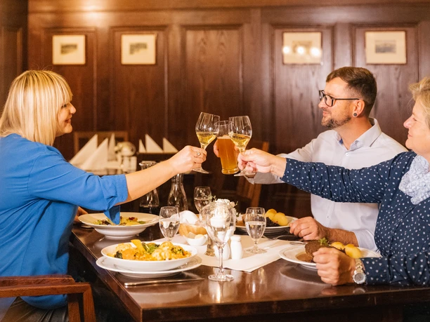 Get-together in Auerbach's cellar - Culinary delights in Leipzig Three guests in Auerbach's cellar clink glasses of wine or beer at a laid table